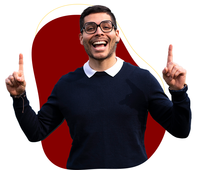 Hombre joven con gafas y jersey oscuro sonriendo y señalando hacia arriba con ambos índices, sobre un fondo decorativo abstracto rojo y amarillo